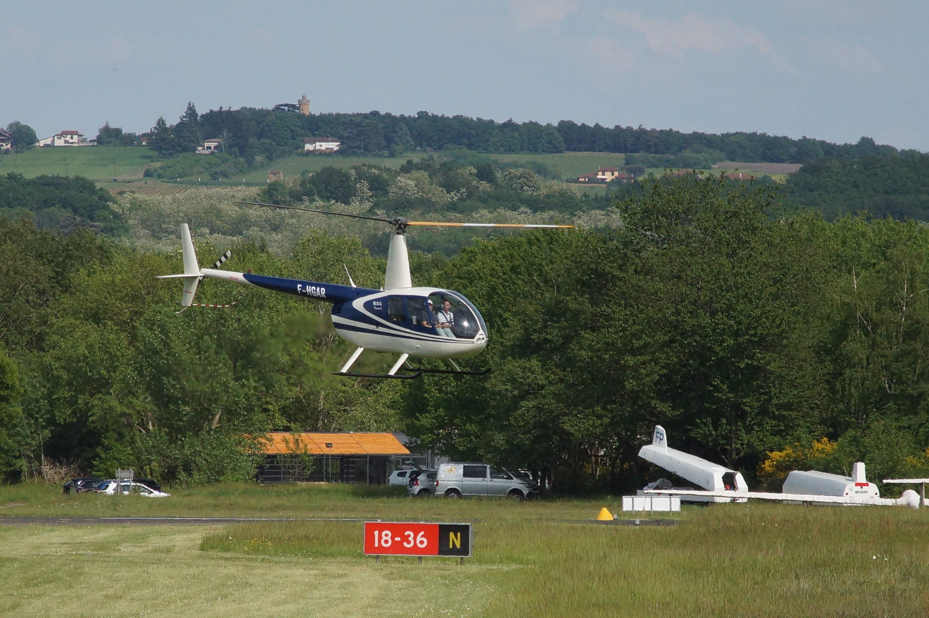 Symbolbild: Robinson R44 im Schwebeflug vor grünen Hügeln